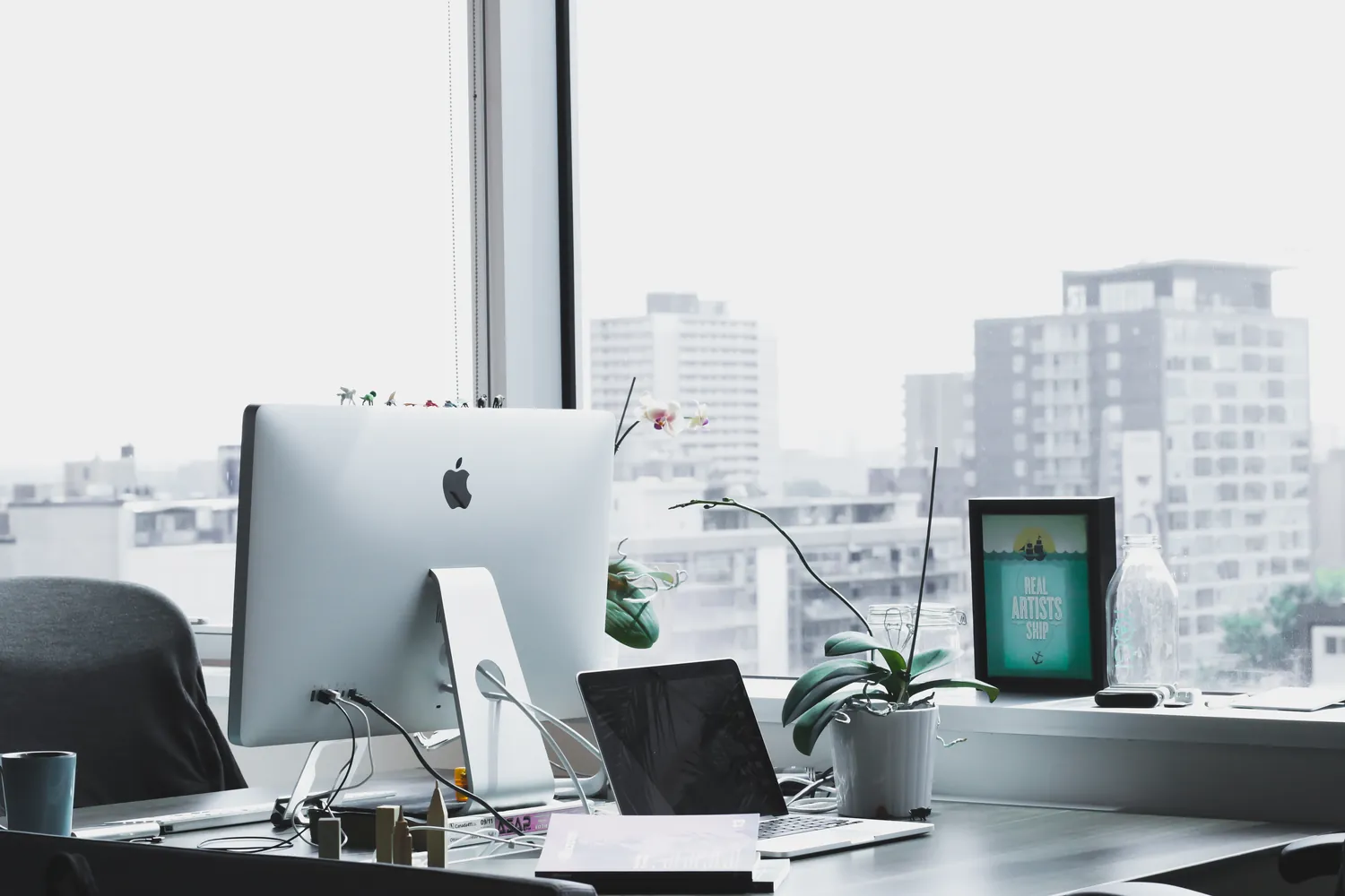 A desk by a window with a computer overlooking a city