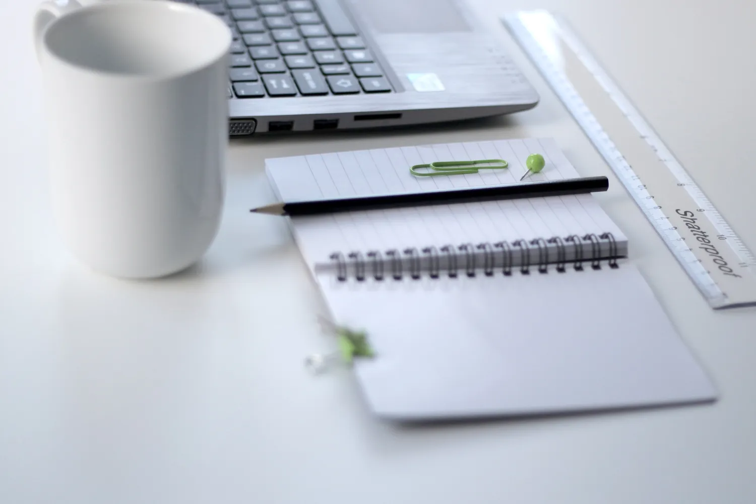 A ruler, notebook, mug and laptop on a white desk