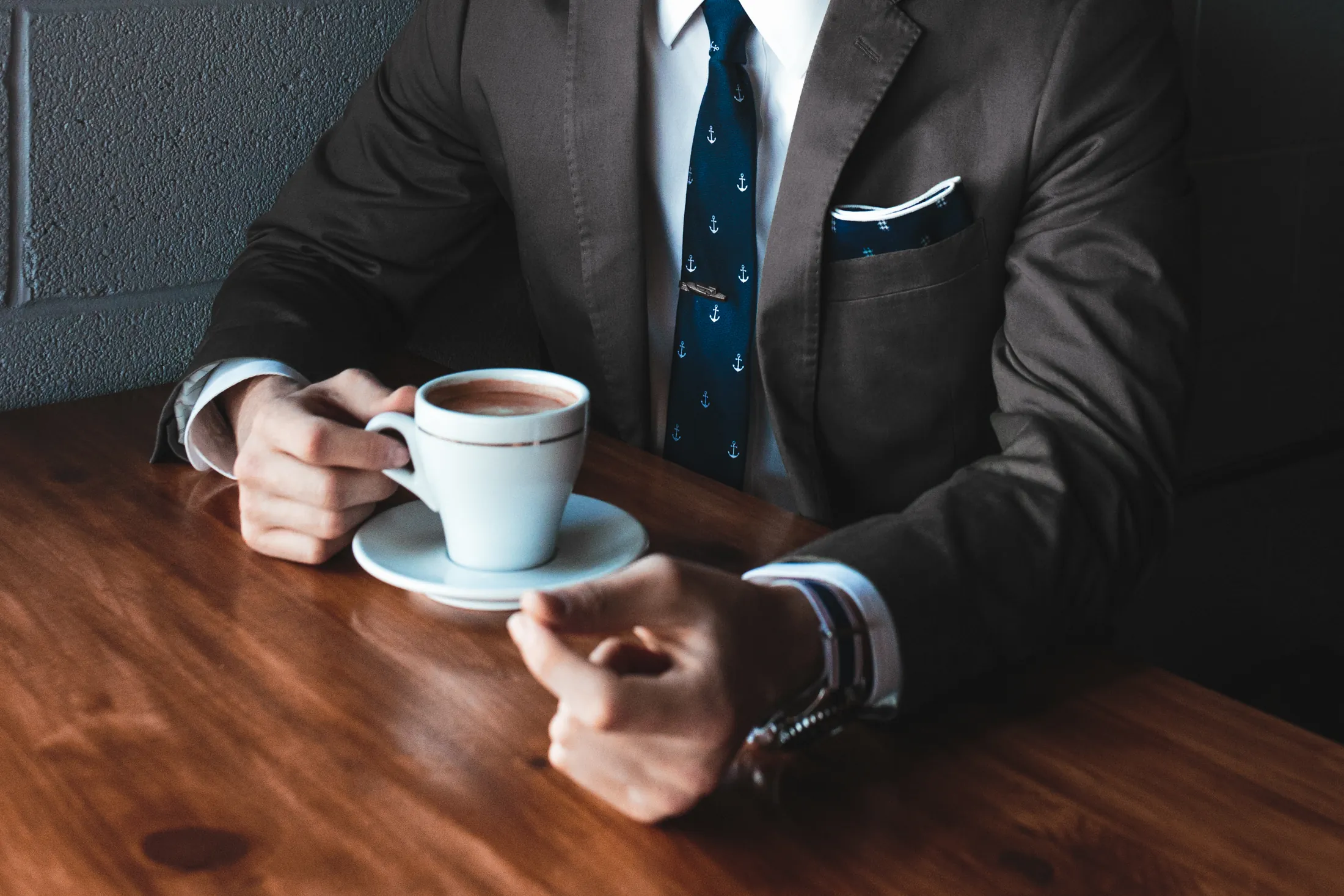 A man in a suit and tie holding a coffee cup at a wooden table