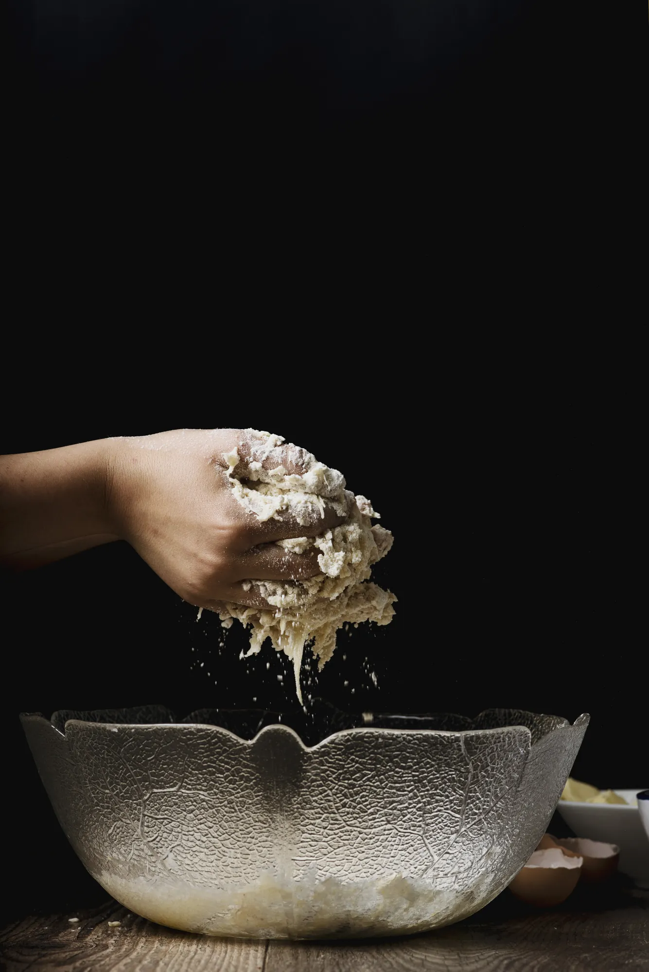 A hand dusting flour over a bowl against a dark background