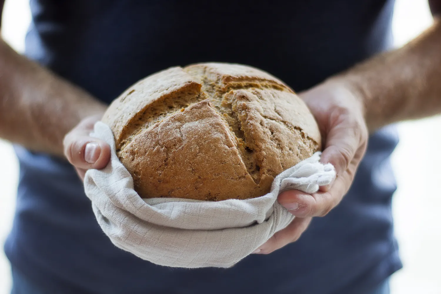 Hands holding a round loaf wrapped in a cloth