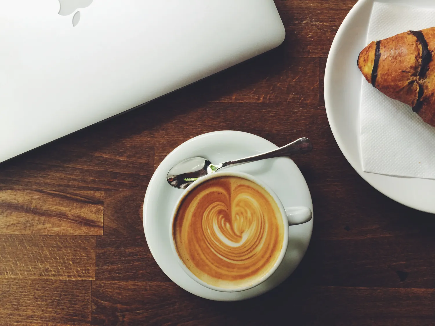 A latte and a croissant on a dark wooden table