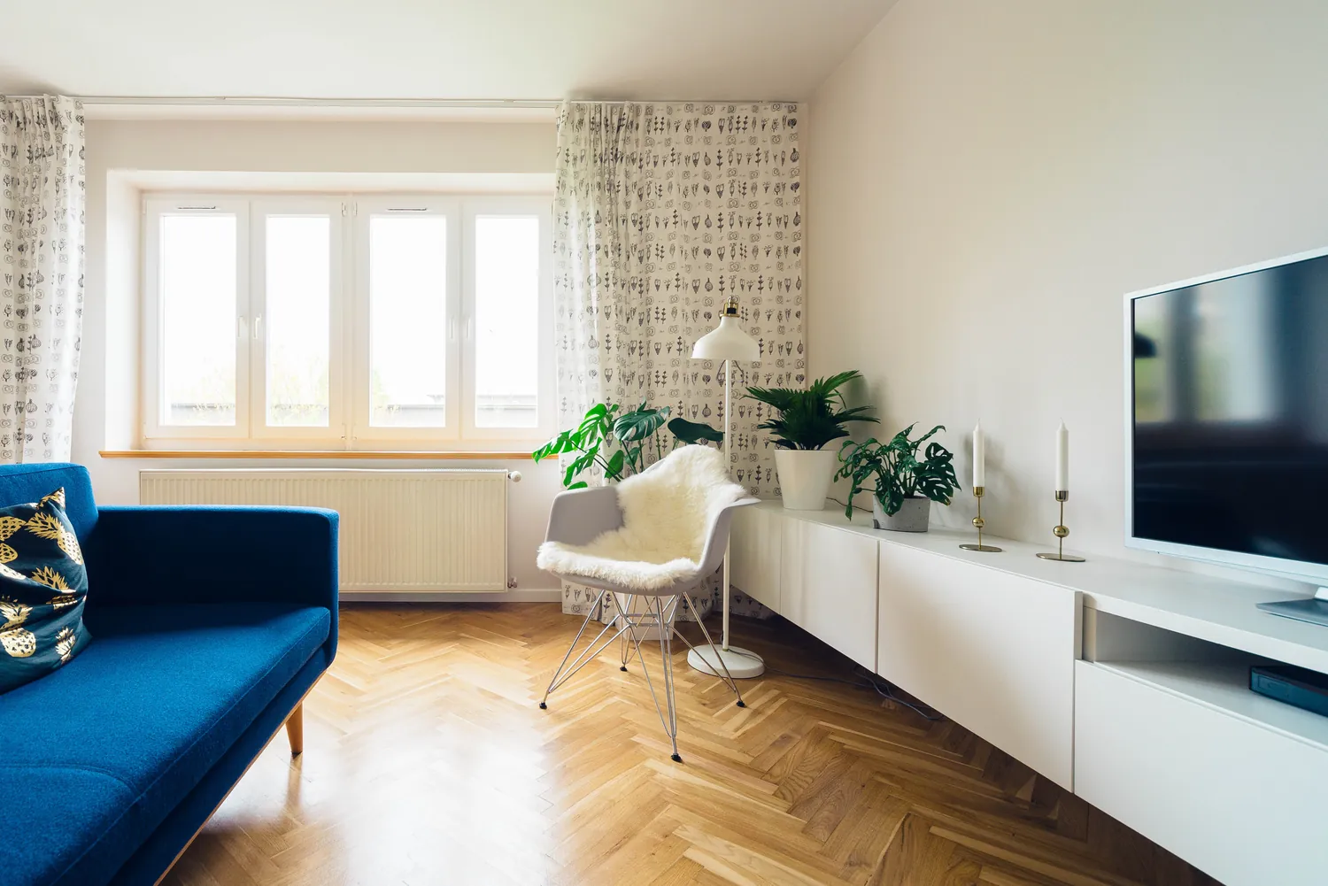 A bright living room with a blue sofa, herringbone floor and white shelving