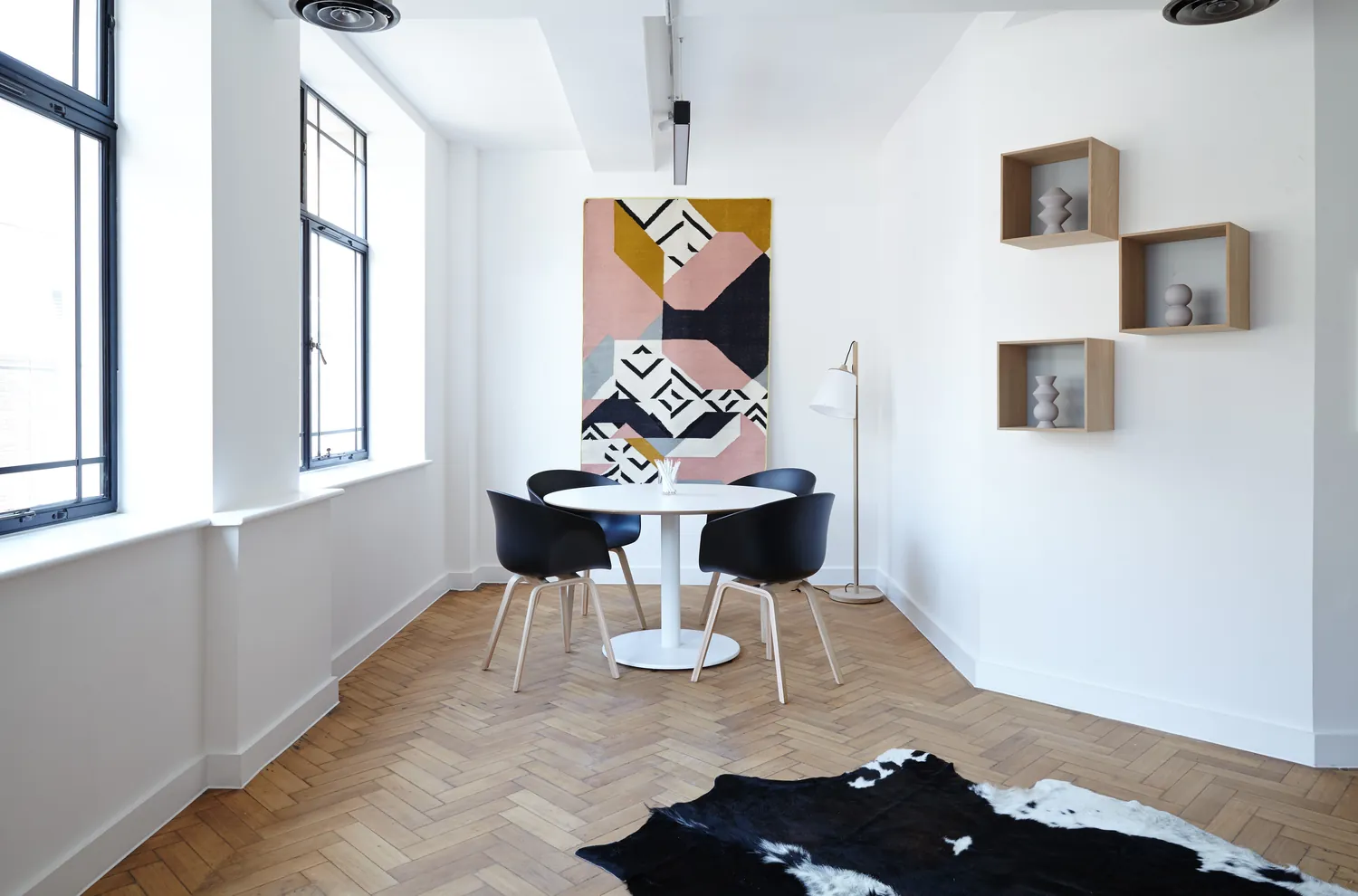 A white room with a round table, black chairs and a herringbone floor