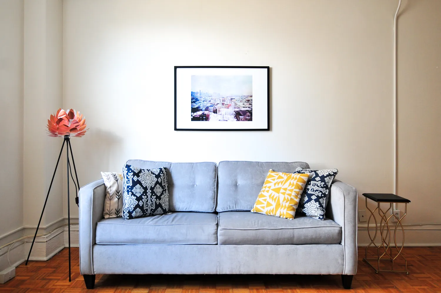A pale blue sofa with patterned cushions beneath a framed print on a white wall