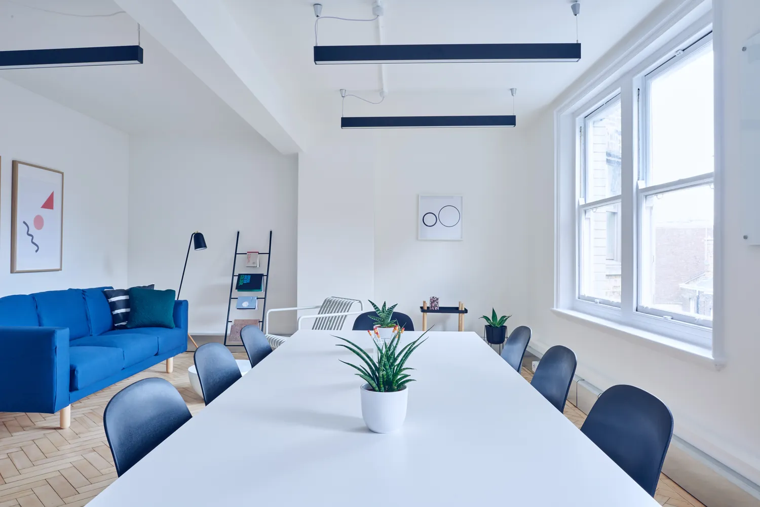 A white room with large windows, a blue sofa and a long table