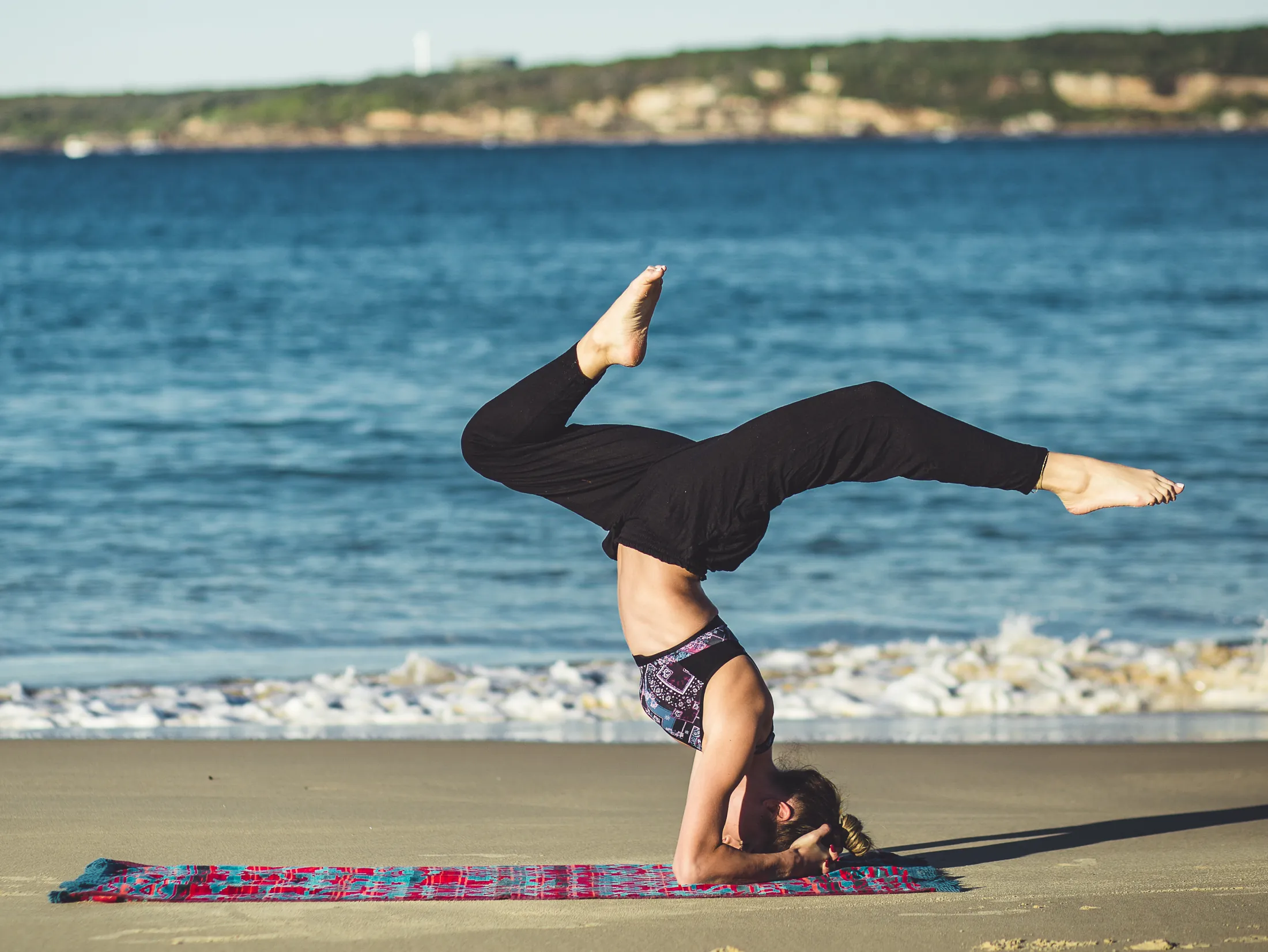 A person in a yoga handstand on a beach mat beside the sea