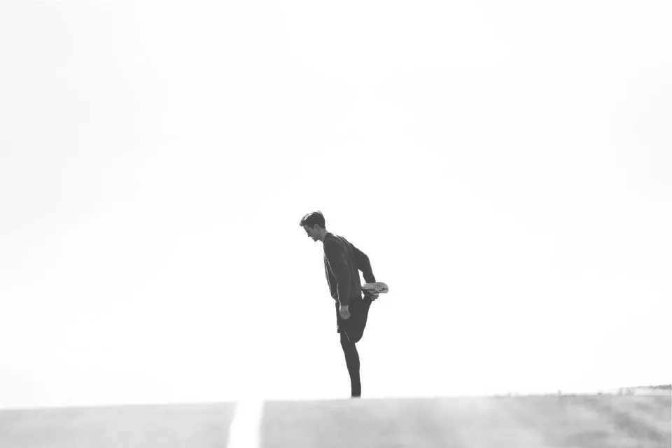 A lone figure stretching a leg against a pale sky