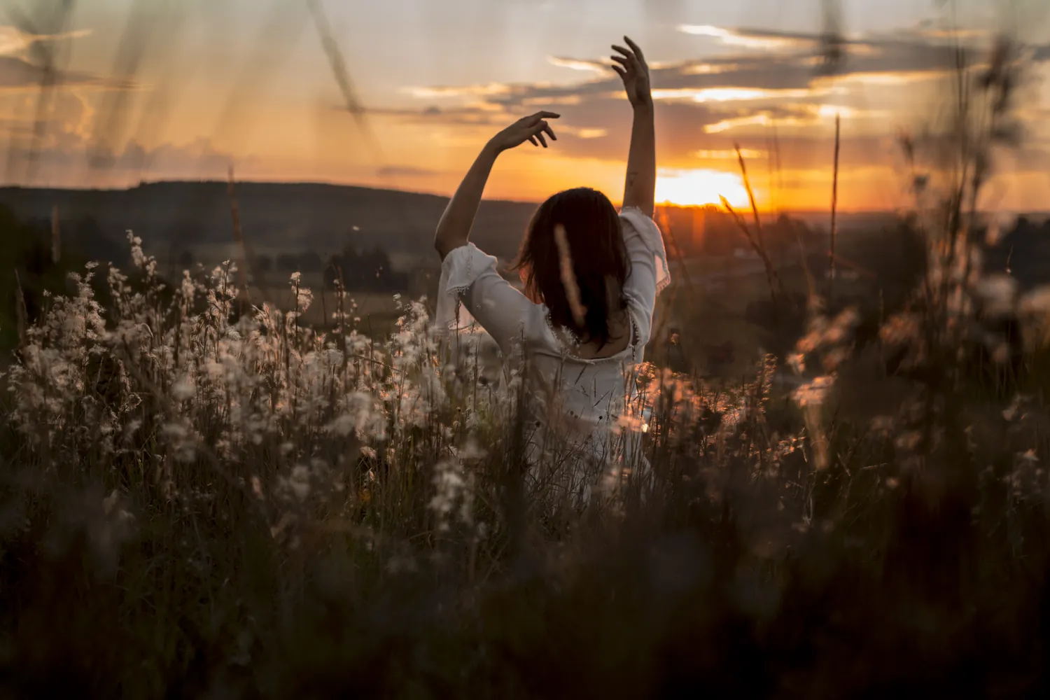 A woman in a yoga pose in tall grass at sunrise