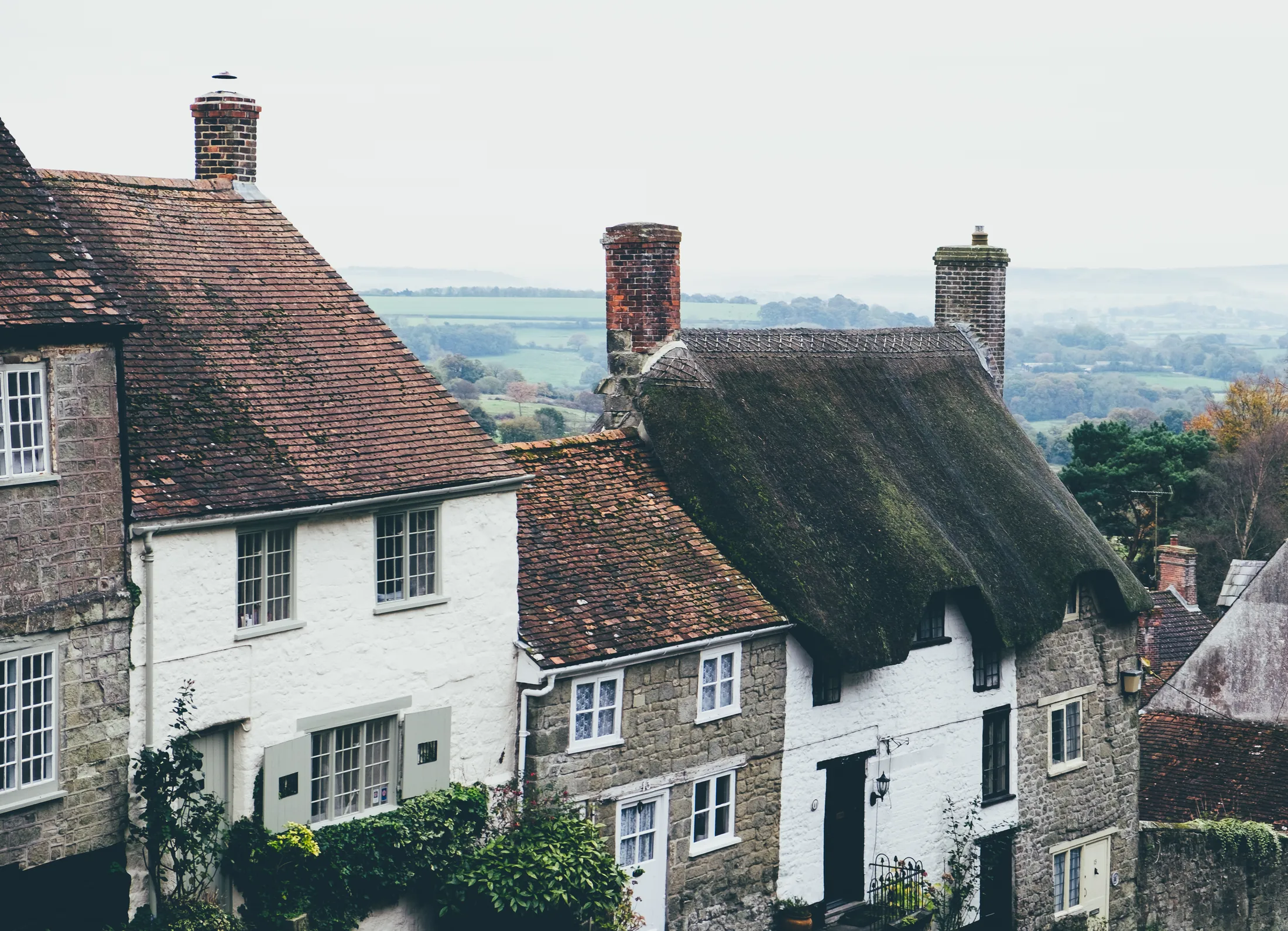 Tiled and thatched roofs with brick chimneys on a hillside street