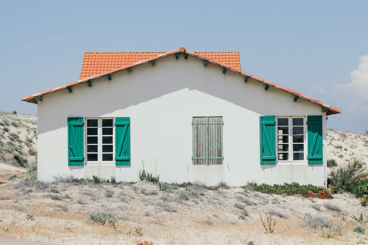 A white house with an orange tiled roof and green shutters