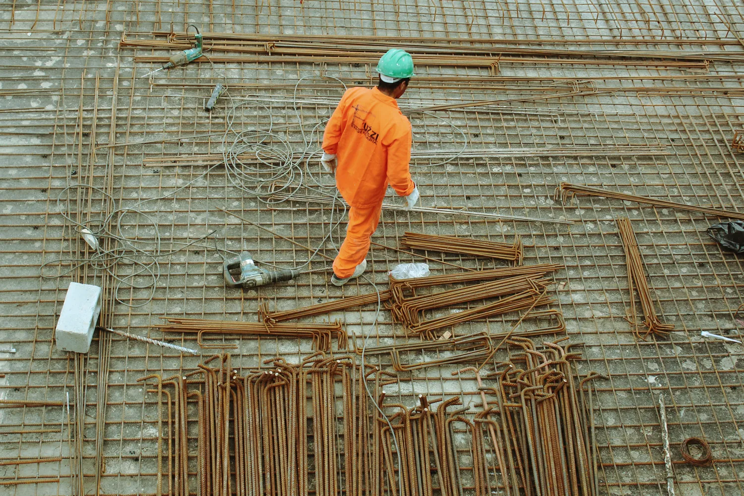 A worker in orange overalls and a hard hat walking across a roof structure