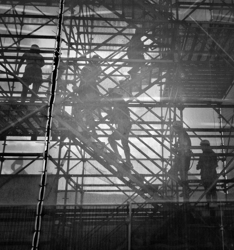 Black and white view of figures moving through building scaffolding